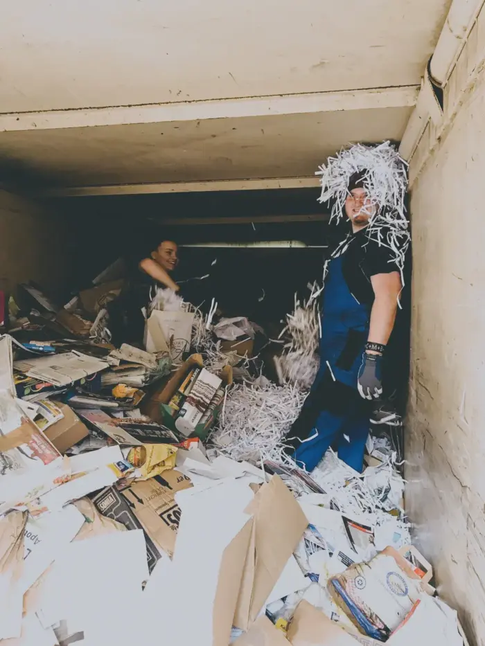 Helfer im Altpapiercontainer lässt sich lachend Schredderpapier über den Kopf regnen.