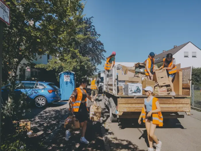 Jugendliche in orangen Warnwesten laden Kartons und Papiertüten auf einen LKW bei der Altpapiersammlung.