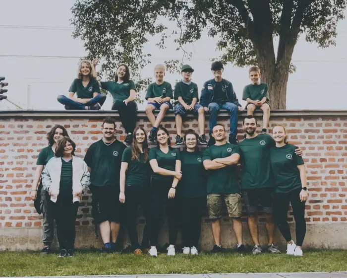 Gruppenfoto der Pfarrjugend in grünen T-Shirts vor einer Ziegelmauer, die obere Reihe sitzt auf der Mauer.
