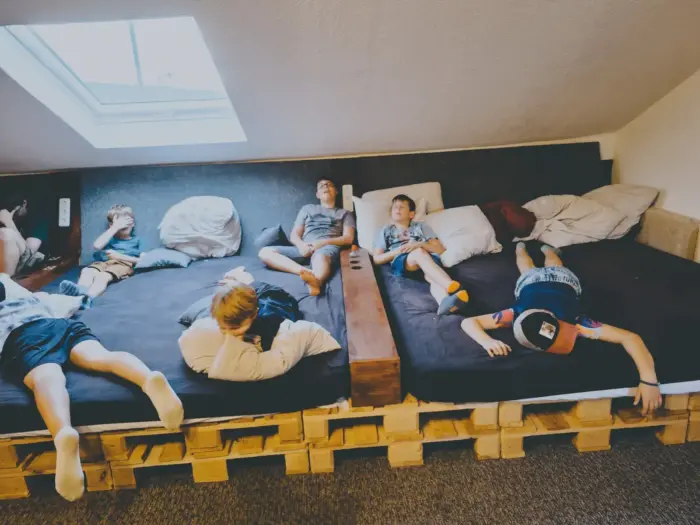 Sieben Kinder liegen entspannt auf einem breiten Palettenbett unter dem Dachfenster im Gruppenraum.