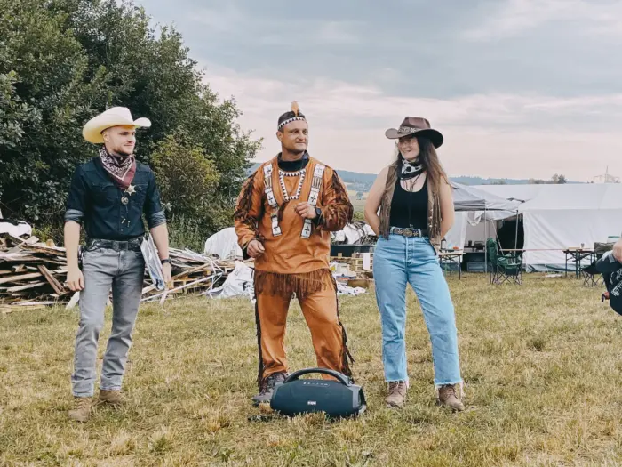 Drei Jugendliche in Wildwest-Verkleidung stehen auf der Lagerwiese, dahinter die Zelte des Lagers.