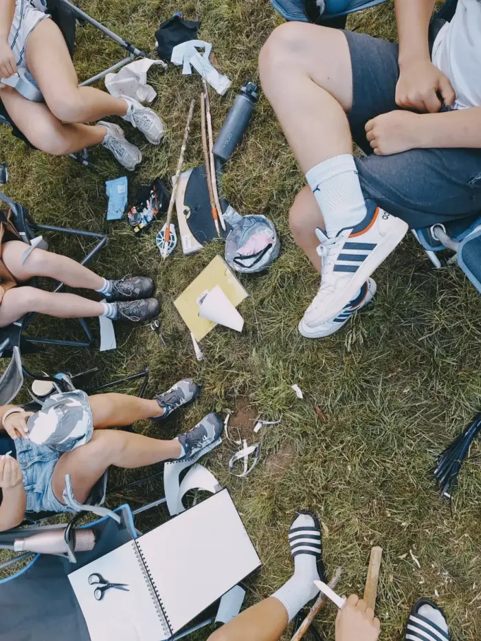Von oben fotografiert: Beine und Schuhe im Kreis auf der Wiese, in der Mitte ein aufgeschlagener Block.
