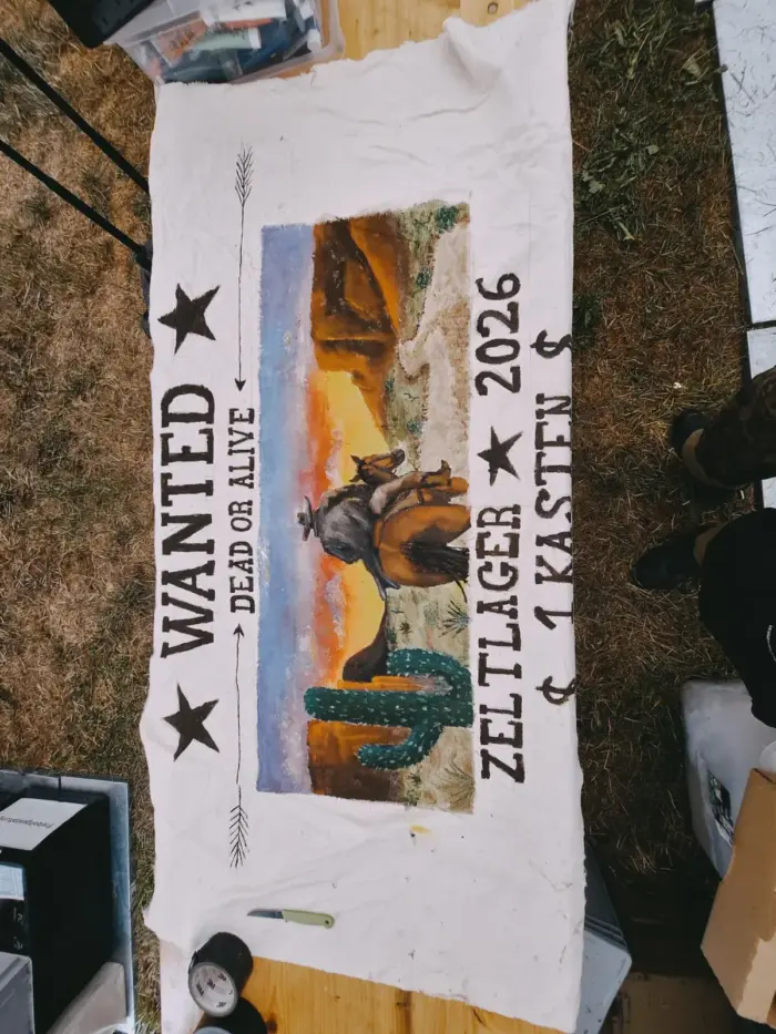 Ein von Hand bemaltes Stofftransparent: WANTED, DEAD OR ALIVE, Zeltlager 2026, daneben eine Wüstenlandschaft mit Kaktus.